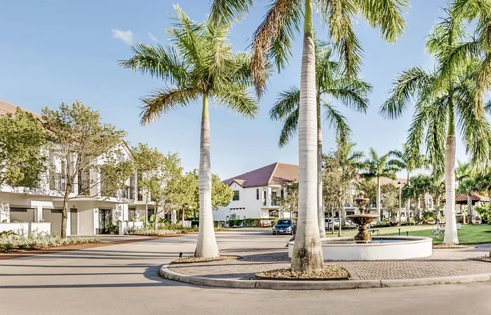 Elegant apartment community with palm-lined streets, modern architecture, and a charming central fountain.