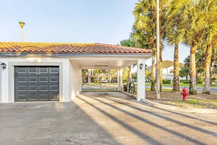 Charming garage with Spanish tile roof and electric vehicle charging station, surrounded by palm trees for a tropical feel.