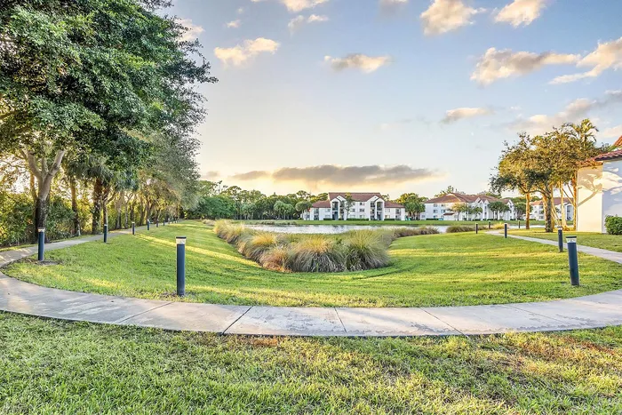 Picturesque apartment complex with spacious green lawns, winding pathways, and serene water view under a beautiful sunset sky.