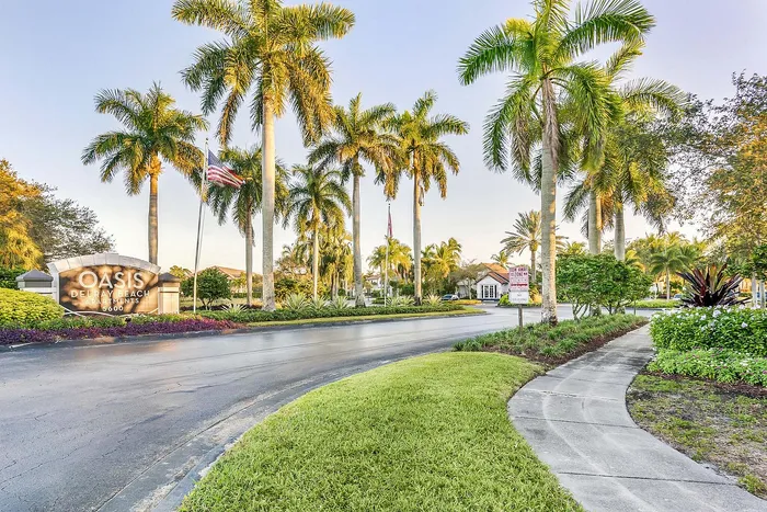 Inviting entrance of Oasis Delray Beach Apartments, adorned with swaying palm trees and lush greenery, showcasing an upscale living environment.