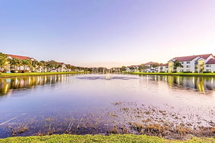 Scenic lakeside view of modern apartment community with elegant architecture and lush greenery at sunset.