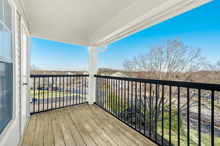 Charming apartment balcony with wooden flooring and black railings offering a panoramic view of a serene suburban landscape.