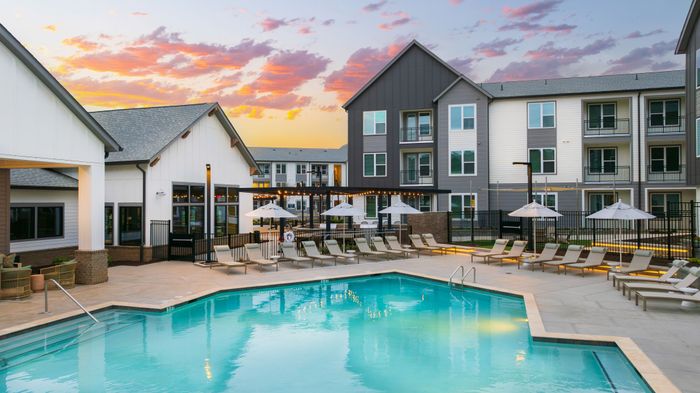 Charming apartment complex showcasing a beautiful swimming pool surrounded by stylish lounge chairs and umbrellas, all set against a vibrant sunset sky.