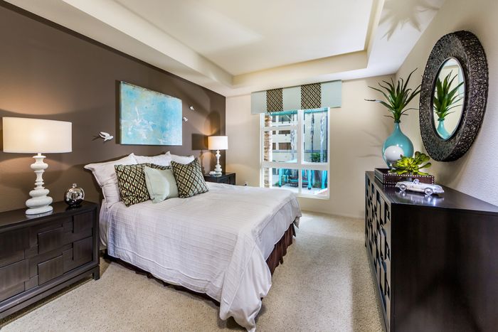 Elegant bedroom with modern decor features a cozy bed, stylish art, and abundant natural light through large windows.