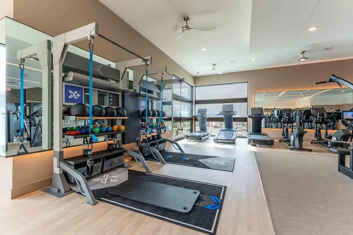 Modern gym with state-of-the-art equipment including treadmills, kettlebells, and a weight rack in a bright, spacious setting.