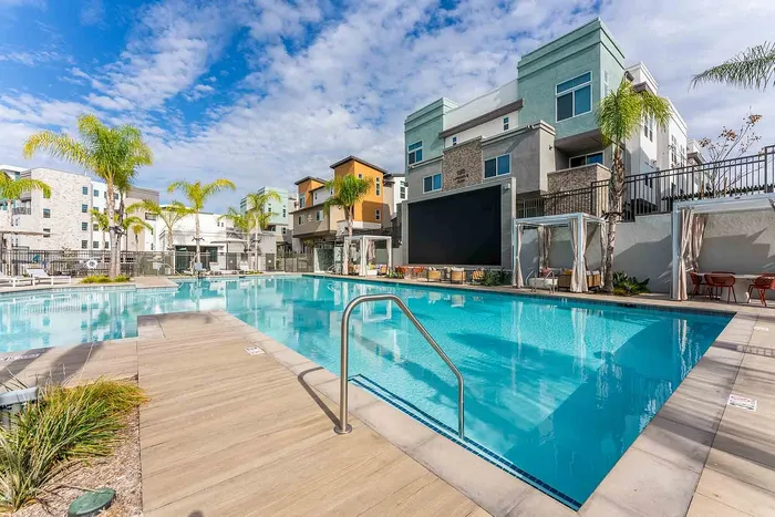 Luxurious outdoor pool area surrounded by modern apartments and lush palm trees under a bright blue sky.