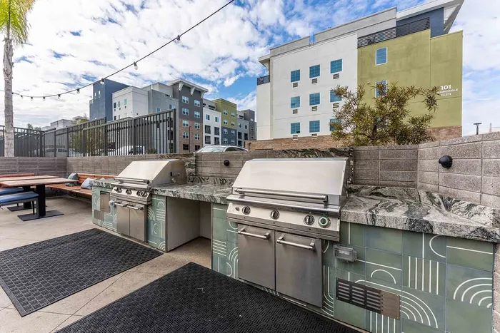 Outdoor lounge with BBQ grills, stylish tile countertops, and urban apartment backdrop.