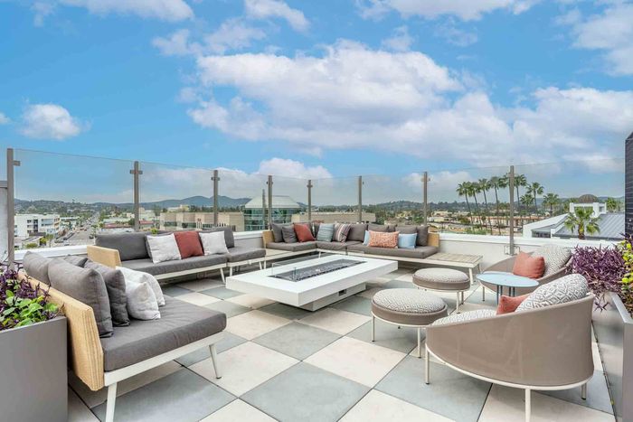Luxurious rooftop terrace with stylish seating, fire pit, and stunning city views under a vibrant blue sky.