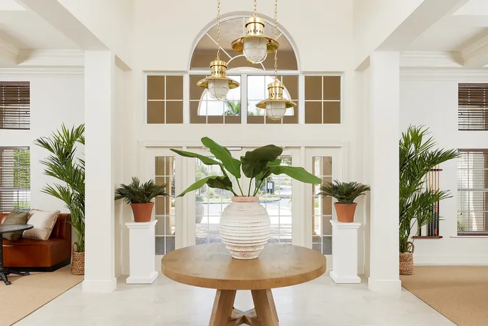 Elegant entryway with luxurious lighting, lush greenery, and a welcoming wooden table centerpiece.