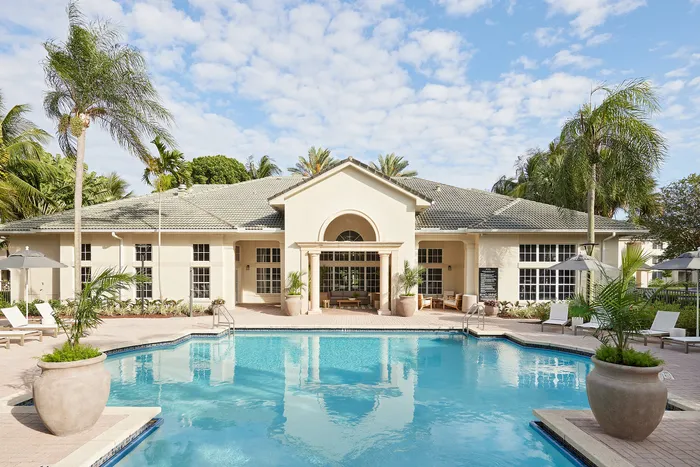 Elegant residential building with luxurious pool surrounded by palm trees, offering a tropical oasis atmosphere.
