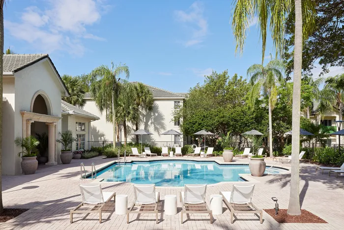 Luxurious apartment complex featuring a crystal-clear pool surrounded by lush palm trees and elegant lounge chairs, perfect for relaxation in a tropical paradise.