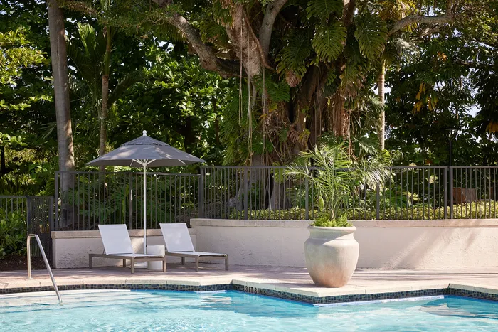 Serene outdoor pool area with lush greenery, comfortable lounge chairs, and a sun umbrella, perfect for relaxation.