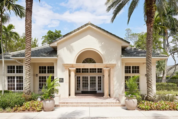 Stunning exterior of a luxurious villa with elegant columns, lush landscaping, and palm trees under a bright blue sky.