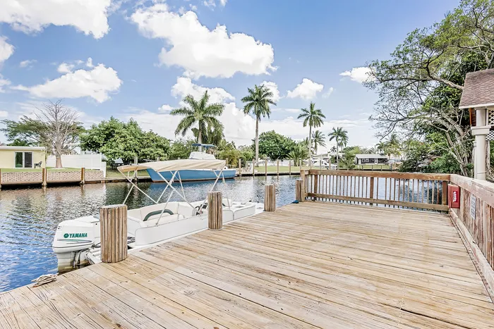 Charming waterfront dock with scenic views, featuring lush palm trees and a tranquil canal ideal for boating.