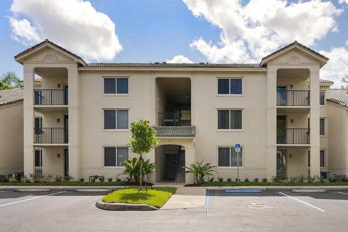 Elegant three-story apartment building with charming balconies, surrounded by lush greenery and bright skies.