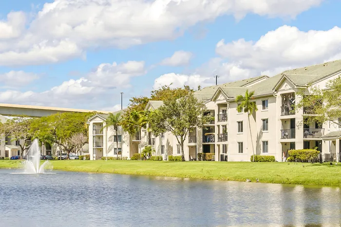 Elegant apartment complex with serene pond view, lush landscaping, and fountain, perfect for tranquil living.