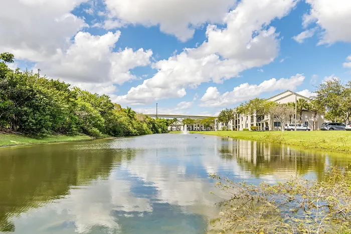 Captivating lakeside view with lush greenery and elegant apartment buildings under a vibrant blue sky with fluffy clouds.