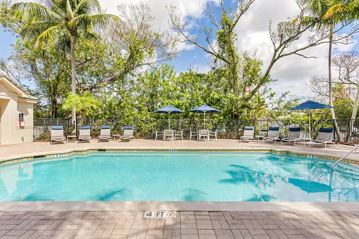 Inviting outdoor pool area surrounded by lush greenery and palm trees, featuring comfortable loungers and chic blue umbrellas for a relaxing escape.