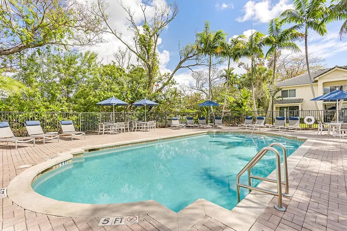 Inviting outdoor pool area surrounded by lush greenery, featuring comfortable lounge chairs and elegant umbrellas, perfect for relaxation.