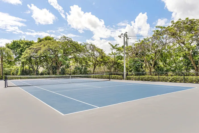 Inviting outdoor tennis court surrounded by lush greenery and a clear blue sky, perfect for sports enthusiasts.