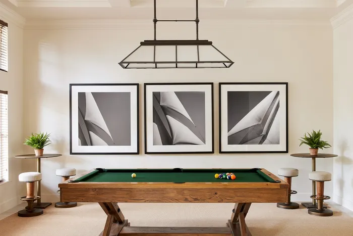 Sophisticated game room with a classic wooden pool table, modern monochrome art pieces, and elegant seating area with potted plants for a stylish ambiance.
