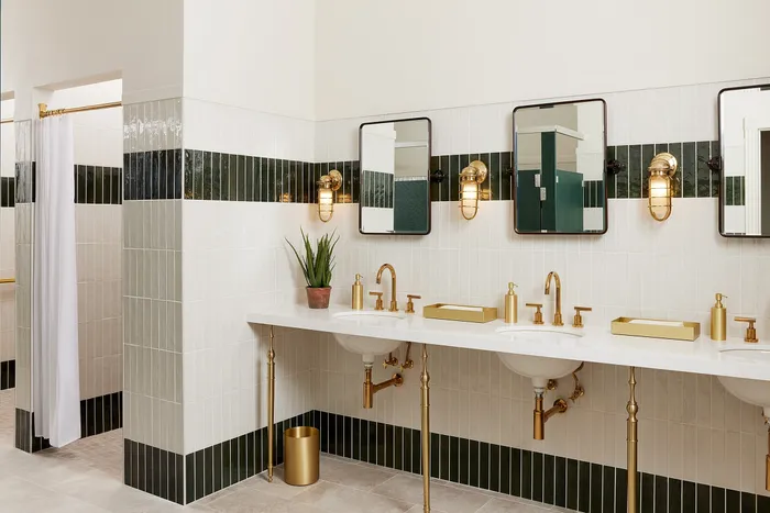 Elegant bathroom with gold fixtures, double sinks, and white tiled walls complemented by a lush green plant.