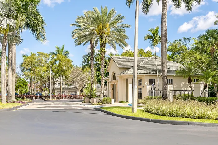 Inviting and lush apartment complex entrance surrounded by palm trees and vibrant greenery under a clear blue sky.