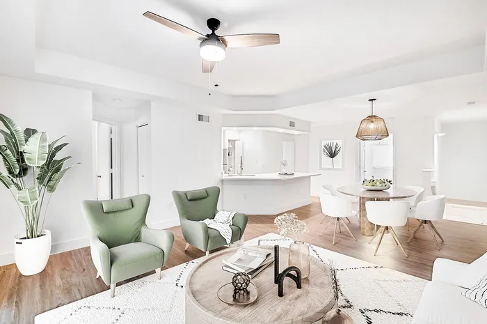 Bright and inviting open-concept living room with elegant green armchairs, modern ceiling fan, and a cozy dining area, perfect for stylish entertaining.