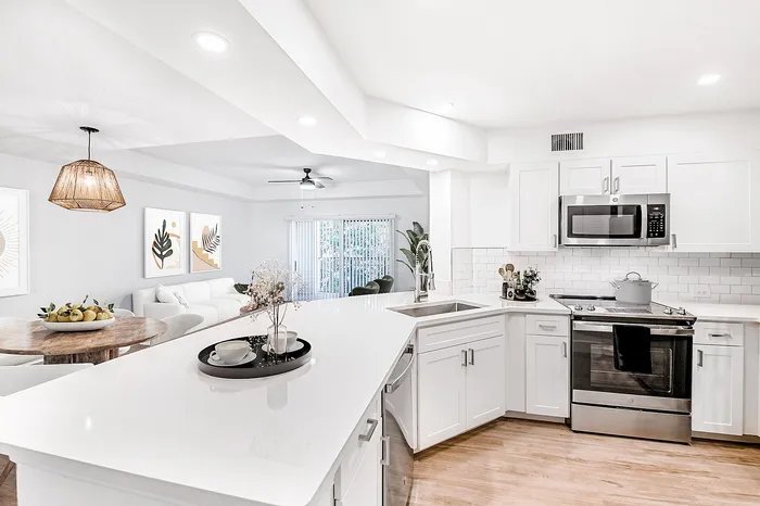 Bright, modern kitchen and living area with sleek white cabinetry, stainless steel appliances, and elegant decor, creating an inviting open-concept space perfect for entertaining.