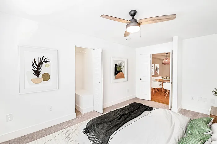 Bright, modern bedroom with stylish decor, featuring a ceiling fan and a glimpse into a warm dining area.