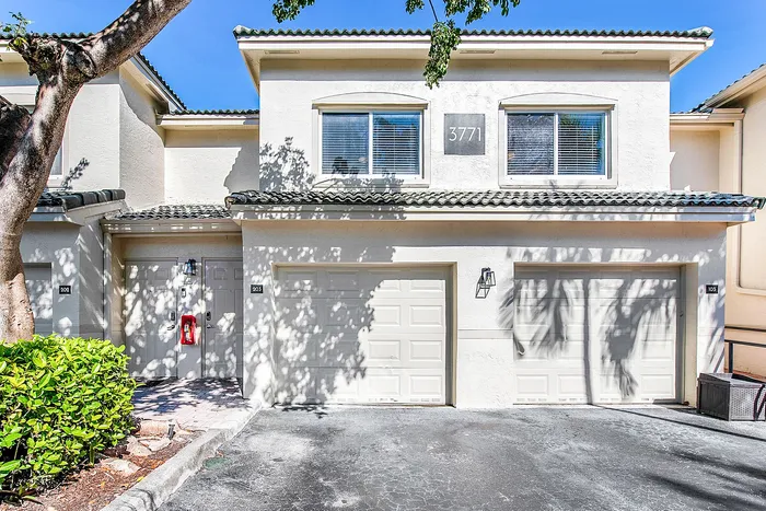 Charming two-story townhouse with a double garage, bathed in sunlight and surrounded by lush greenery.