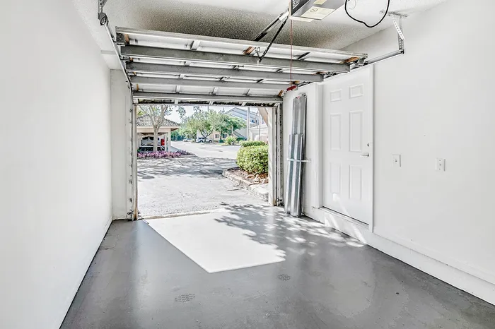 Bright and inviting garage with ample space, open door view to a sunny driveway and greenery, enhancing the appeal of suburban living.