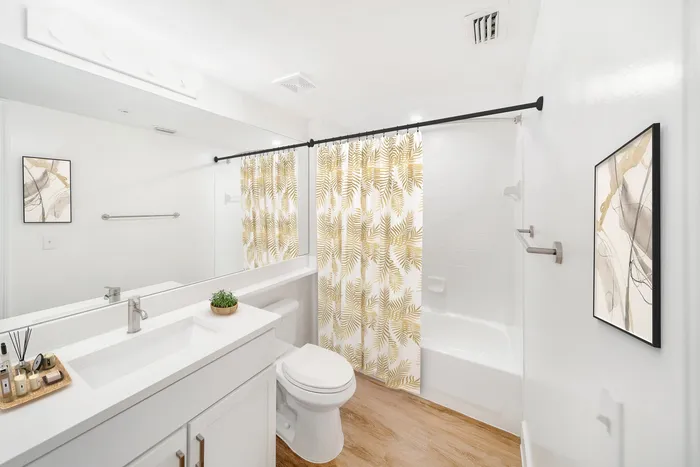 Bright, modern bathroom with sleek fixtures, stylish abstract art, and elegant gold leaf-patterned shower curtain.
