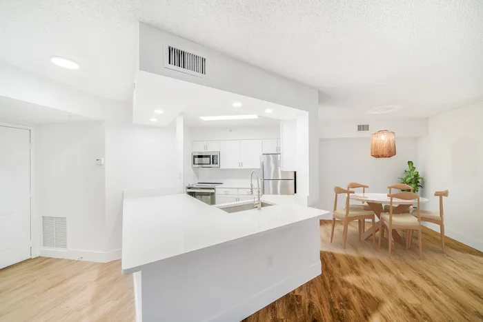 Bright, modern kitchen and dining area featuring sleek white cabinetry, stainless steel appliances, and wood-accented flooring, perfect for stylish living.