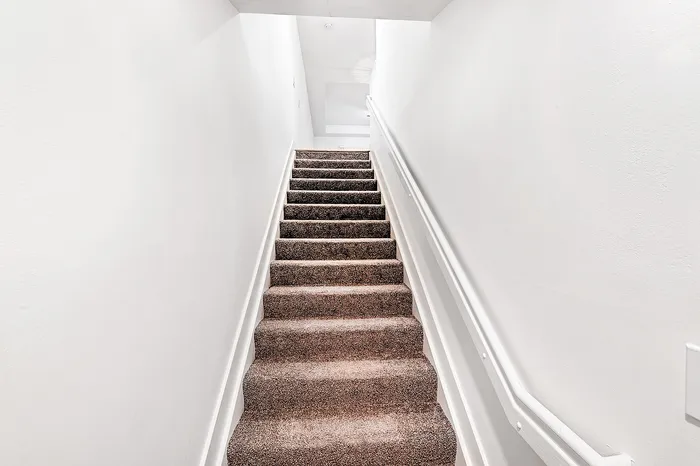 Inviting carpeted stairway with bright white walls, leading to a cozy upper space in a modern apartment.