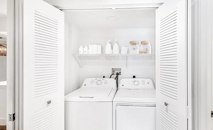 Chic and modern laundry space featuring a washer and dryer tucked behind stylish white louvered doors, complemented by organized shelving and neatly arranged essentials.
