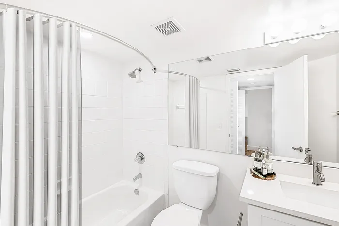 Bright and elegant bathroom featuring a pristine white bathtub with a sleek curved shower rod, modern vanity sink, and ambient lighting, creating a tranquil oasis.
