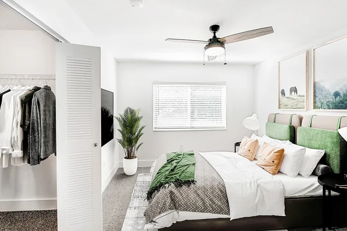 Bright, modern bedroom with a cozy bed, elegant decor, and spacious closet. Features a ceiling fan, stylish artwork, and natural light from a large window.