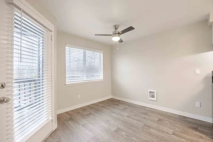 Bright and airy room featuring sleek hardwood flooring, large windows with blinds, and a modern ceiling fan, perfect for a cozy and refreshed living space.