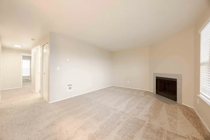 Bright and inviting living space featuring plush carpet, a cozy fireplace, and ample natural light from large windows.