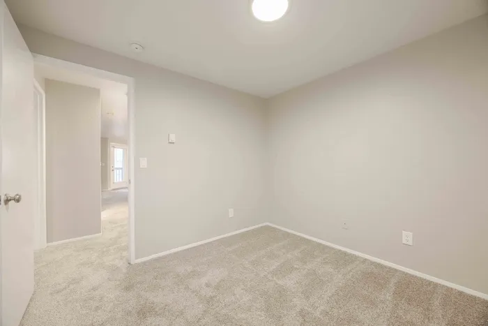 Bright, cozy room with soft carpet flooring and open doorway leading to a sunlit space. Ideal for stylish living.