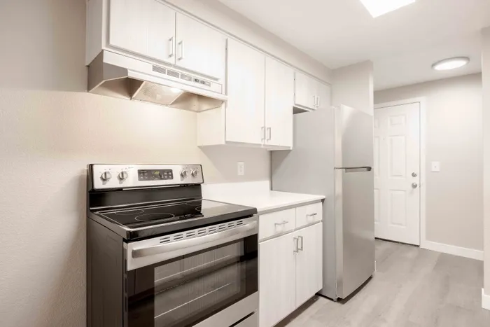Bright, modern kitchen with sleek stainless steel appliances, pristine white cabinetry, and stylish wood flooring, perfect for culinary creativity.