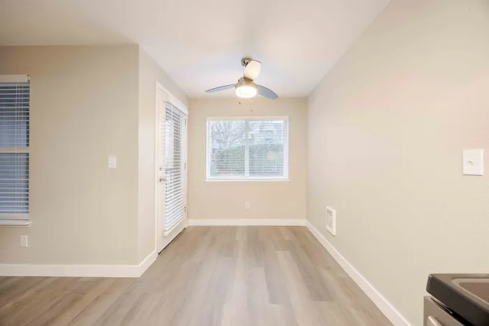 Bright and spacious room with light wood flooring, modern ceiling fan, and large windows providing natural light.