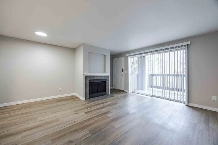 Bright and inviting living room with sleek wood flooring, modern fireplace, and large sliding glass doors leading to a serene balcony.