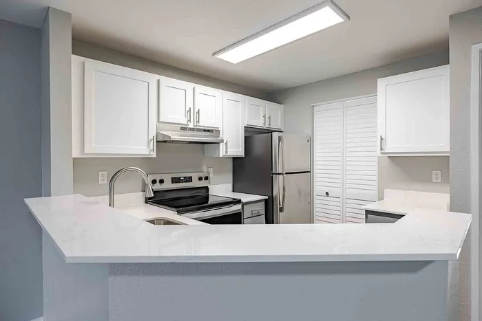Modern kitchen with sleek white cabinets, stainless steel appliances, and a spacious marble countertop.