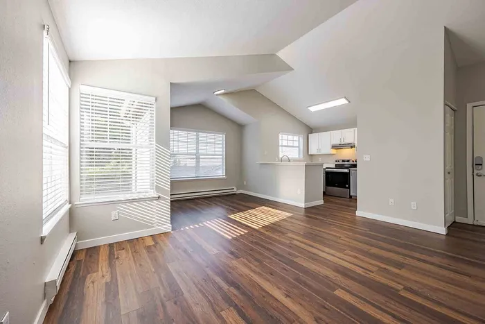 Bright and airy apartment interior with elegant wood flooring, large windows, and modern kitchen boasting sleek white cabinetry.