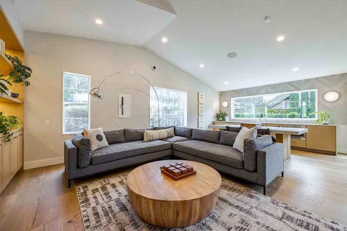 Contemporary open living space with a cozy L-shaped sofa, stylish wooden coffee table, and large windows offering abundant natural light.