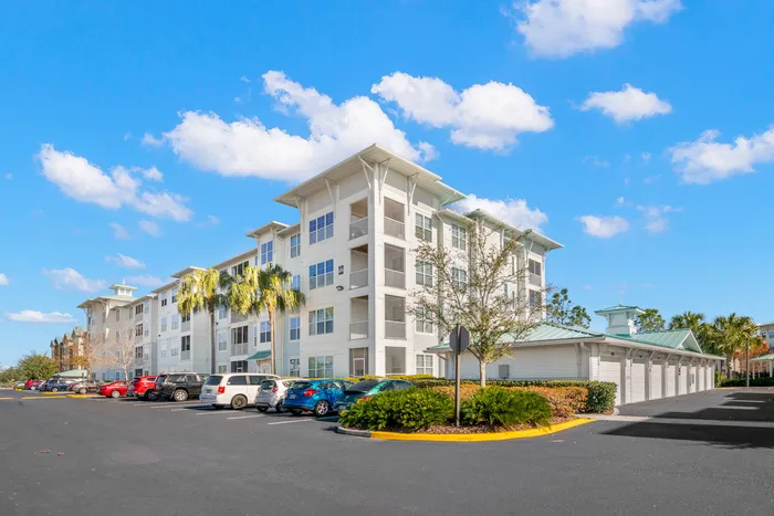 Contemporary apartment complex with vibrant exterior, ample parking, and lush landscaping under a clear blue sky.