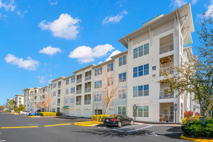 Elegant modern apartment building basking in sunlight, showcasing spacious balconies and well-maintained greenery under a clear blue sky.