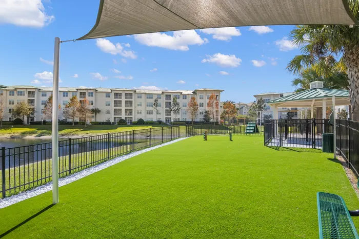 Charming apartment complex with lush green lawns, a serene pond, and a welcoming gazebo under a sunny blue sky.